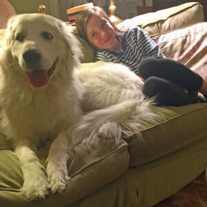 A young girl and her fluffy white dog snuggle up on the couch together